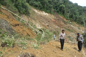 Kasat Lantas, AKP. Arie Sofandi Paloh dengan latar belakang longsor. Diatas alat berat inilah jalan darurat dengan seutas rotan yang dilintasi masyarakat. Bila terpeleset ke bawah, ancamannya maut. (Foto/Dok Lantas Aceh Tengah)